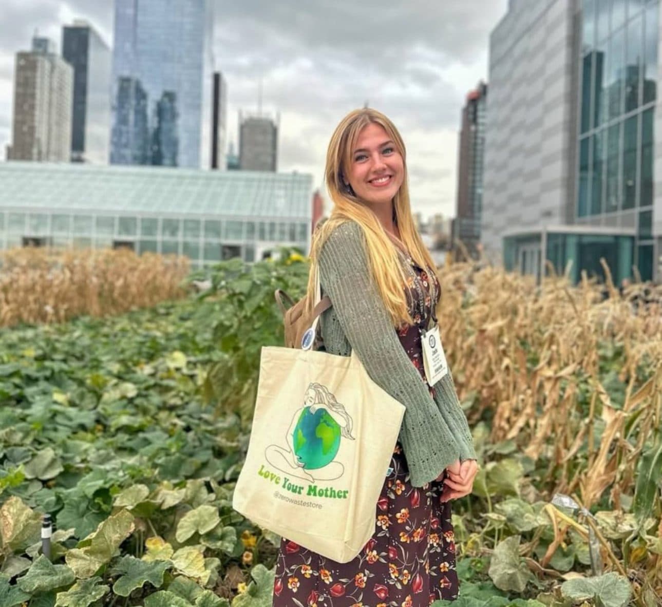 Jade Banham standing among squash vines and dried corn on a rooftop farm, with the Manhattan skyline behind her